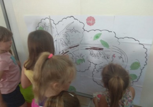 Zdjęcie przedstawia grupę dzieci, które malują farbami, wcześniej ułożone z papierowych puzzli drzewo